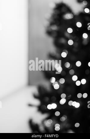 Eine vertikale schwarze und weiße Bokeh Hintergrund erstellt durch eine Reihe von defokussierten Lichter auf der einen Seite eines Weihnachtsbaumes. Stockfoto