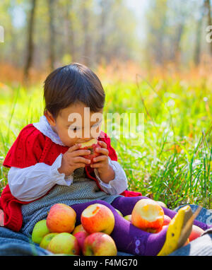 Kind mit roten Äpfeln sitzt auf Blätter im Herbst park Stockfoto