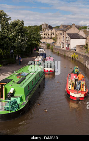 Sonnige Sommer, Ansicht des Menschen entspannen auf Kanal Leinpfad, Boote vertäut & 1 Mann Lenkung Boot entfernt - Leeds-Liverpool Kanal, Skipton, Yorkshire, England. Stockfoto