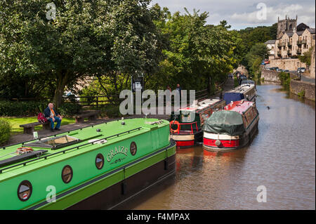 Sonnige Sommer, hohe Aussicht auf Kanalboote festgemacht und Menschen entspannen am Leinpfad - Federn Branch, Leeds-Liverpool Kanal, Skipton, Yorkshire, England. Stockfoto