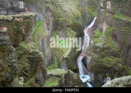 Person durch einen Wasserfall in der Fjadrargljufur Canyon, Sudhurland, Island in den Schatten gestellt. Stockfoto