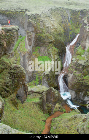 Person durch einen Wasserfall in der Fjadrargljufur Canyon, Sudhurland, Island in den Schatten gestellt. Stockfoto