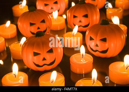 Kleines Spielzeug in Halloween Kürbisse umgeben von orange Teelicht Kerzen Stockfoto