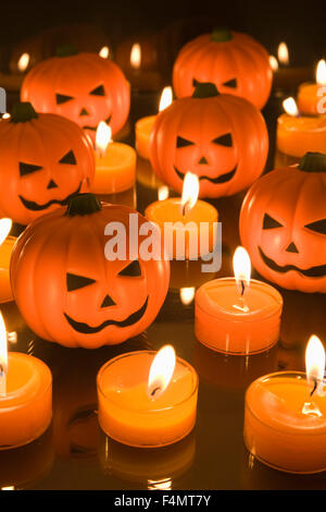 Kleines Spielzeug in Halloween Kürbisse umgeben von orange Teelicht Kerzen Stockfoto