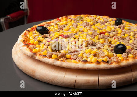 Pizza auf einer Holzplatte mit Thunfisch und Mais, schwarze Oliven Stockfoto