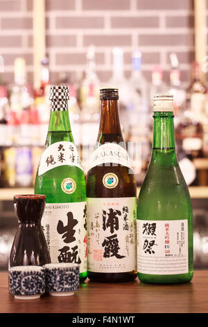 Eine Reihe von japanischen Saki Flaschen auf einer Leiste oben mit Sake-Gläser Stockfoto