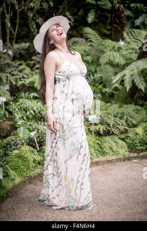 Porträt der schwangeren Frau trägt Sommerkleid und Hut in einem Gewächshaus stehen Stockfoto