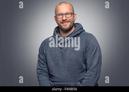 Freundliche attraktive Glatze Mann in Gläsern, betrachtet man die Kamera mit einem schönen warmen Lächeln, Oberkörper grau mit einem highlight Stockfoto