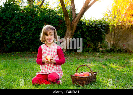 Porträt der lächelnde Mädchen sitzen auf einer Wiese mit Wickerbasket Äpfel Stockfoto