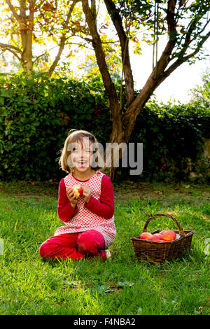 Porträt der lachende Mädchen sitzen auf einer Wiese mit Wickerbasket Äpfel Stockfoto