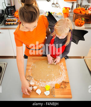 Blonde Mädchen in Fledermaus Kostüm mit Mutter in eingerichteten Küche, Halloween Kekse aus gerollten Teig. Traditionelle Herbstferien Stockfoto