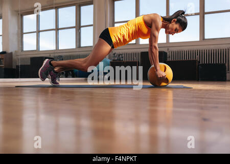 Passen Sie die junge Sportlerin, die auf ihre Rumpfmuskulatur trainieren. Muskulöse Frau Ausübung auf Fitness-Matte doing Push-ups mit Kettlebel Stockfoto