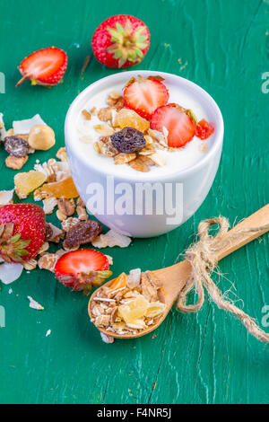 Joghurt mit Müsli Müsli, frische Erdbeeren, Banane und Rosinen in Schüssel auf hölzernen Hintergrund Stockfoto