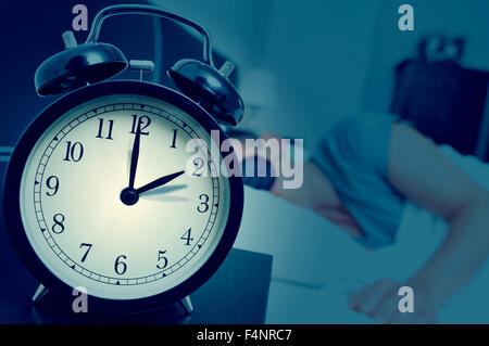 Nahaufnahme eines Weckers auf einem Nachttisch rückwärts eine Stunde am Ende der Sommerzeit anpassen, während ein junger Mann in schläft Stockfoto