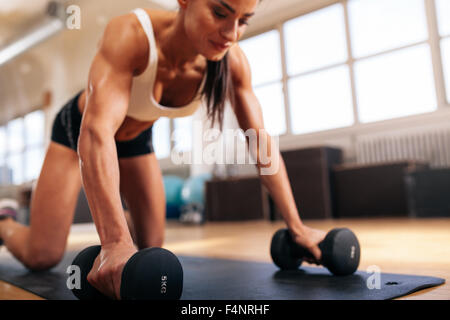 Frau Liegestütze auf Hanteln im Fitnessstudio, Schwerpunkt der armen Frau zu tun. Stockfoto