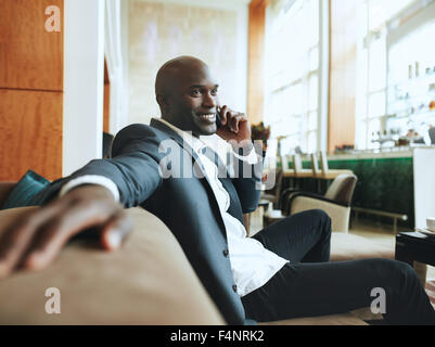 Glücklicher junge Geschäftsmann sitzt entspannt auf Sofa in der Hotellobby einen Anruf tätigen wartet auf jemanden. Stockfoto