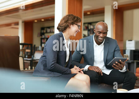 Aufnahme von zwei Personen auf einem Touchscreen-Computer auf etwas blicken. Geschäftsleute, die mit digital-Tablette beim Sitzen am Lächeln Stockfoto