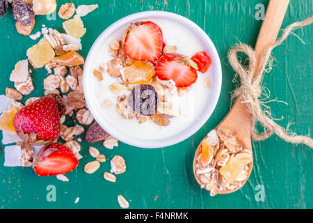 Joghurt mit Müsli Müsli, frische Erdbeeren, Banane und Rosinen in Schüssel auf hölzernen Hintergrund Stockfoto