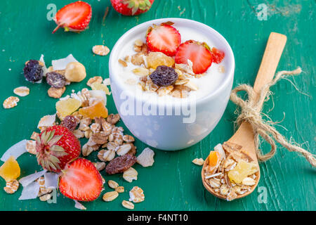 Joghurt mit Müsli Müsli, frische Erdbeeren, Banane und Rosinen in Schüssel auf hölzernen Hintergrund Stockfoto