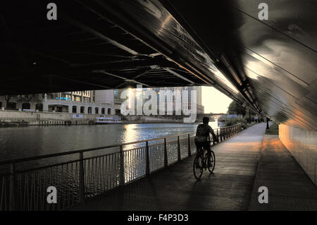 Ein Radfahrer, der Pedale auf den Riverwalk, die im Rahmen der Chicago Michigan Avenue Bridge in Richtung Sonnenaufgang auf einem frühen Sommermorgen. Chicago, Illinois, USA. Stockfoto