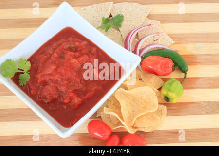 Schüssel mit Tomaten-Salsa mit hot spicy Paprika mag, Jalapeños, Zwiebeln, Chips und Tortillas zum Dippen Stockfoto