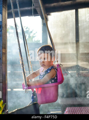 Kleines Mädchen auf einer Schaukel, umgeben von Rauch im Garten Stockfoto