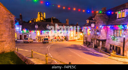 Blick auf die beleuchtete Ruine Corfe Castle in Dorset, Großbritannien mit Weihnachtsbeleuchtung schmücken das Dorf unterhalb. Stockfoto
