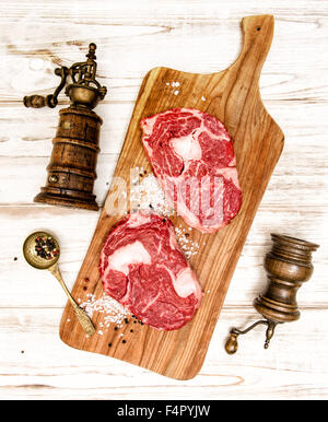 Rohes Frischfleisch Ribeye Steak mit Küchenutensilien auf Schreibtisch aus Holz. Gabel und Messer zur Zubereitung von Speisen Stockfoto