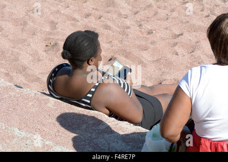Überprüfung ihres Mobiltelefons Frau saß auf dem Sand am Strand von Oddicombe in Torquay, Devon, England Stockfoto