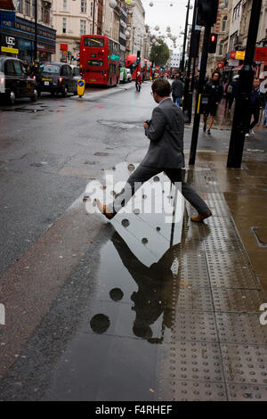 Ein Mann tritt in eine Pfütze nach Regenfällen im Zentrum Londons Oxford Street. Stockfoto