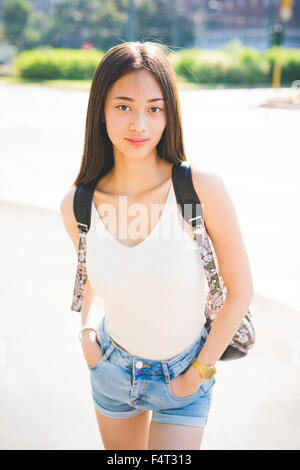 Knie-Figur junge hübsche asiatische lange braune glatte Haare Frau posiert in der Stadt, Hände in Tasche, in der Kamera suchen, lächelnd - Sorglosigkeit, Jugend, Glück-Konzept Stockfoto