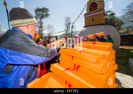 Mann, der tibetische Gebetsbücher verteilt, in gelbes Material gehüllt beim Lhapab Tuchen Festival Stockfoto