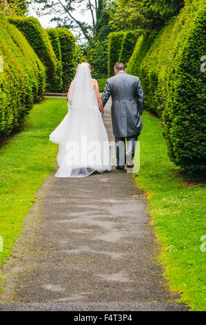 Braut und Bräutigam zu Fuß auf einem Weg in einem Park nach der Heirat. Stockfoto