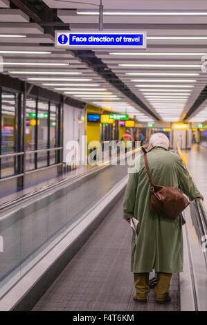 Ein älterer Mann steht auf einem Flughafen travelator. Stockfoto