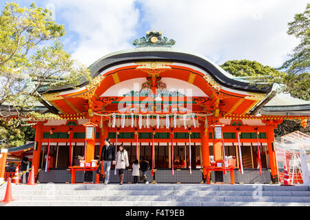 Japan, Koyto, Fushimi. Berühmte Inari Schrein. Main vermilion Shintō-Halle, mit einigen Menschen, die beten vor.. Strahlender Sonnenschein. Stockfoto