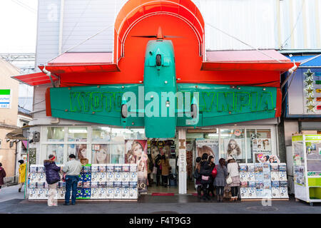 Japan, Kyoto. Beauty Store, bei der die Zeile der süßen, Getränkeautomat, candy Maschinen außerhalb, und die Hälfte ein grünes Flugzeug hängt über dem Eingang mit roten Sonnenschirm. Stockfoto