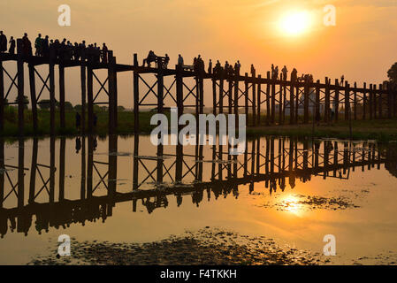 Einheimische und Touristen gehen über die berühmte 1,2 Kilometer lange U Bein Teak Bridge SpanningTaungthaman Lake bei Sonnenuntergang Amarapura, nr Mandalay, Myanmar Stockfoto