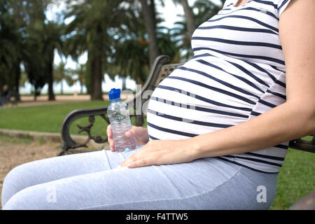 Schwangere Frau im Freien mit Flasche Wasser. Sie sitzt im park Stockfoto