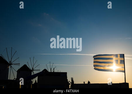 Mykonos Windmühlen bei Sonnenuntergang mit griechischer Flagge im Vordergrund. Stockfoto