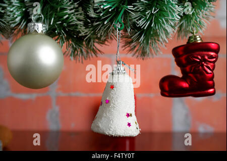 hängen Weihnachtskugeln am künstlichen Fichte Zweig gegen Mauer Stockfoto