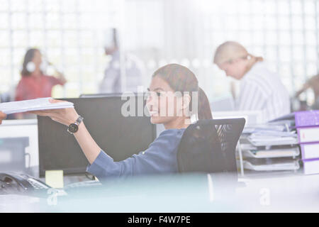 Lächelnde Geschäftsfrau hält Papierkram am Schreibtisch im Büro Stockfoto