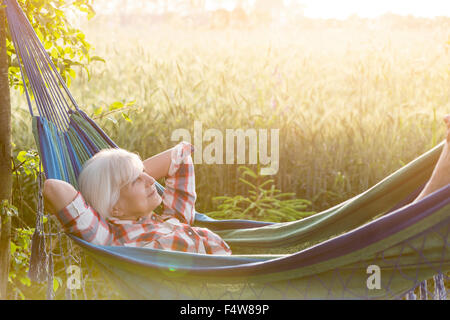 Heitere senior Frau in Hängematte neben ländlichen Weizenfeld Verlegung Stockfoto