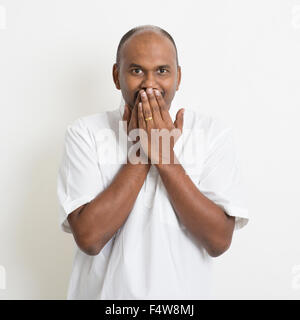 Porträt von Reifen casual Business indischer Mann bedeckt Mund, stehend auf einfarbigen Hintergrund mit Schatten. Stockfoto