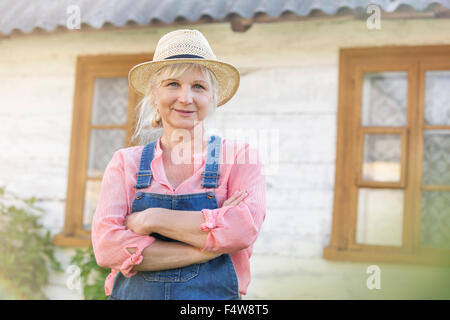 Porträt lächelnd Landwirt in Overalls und Strohhut außerhalb Bauernhaus Stockfoto