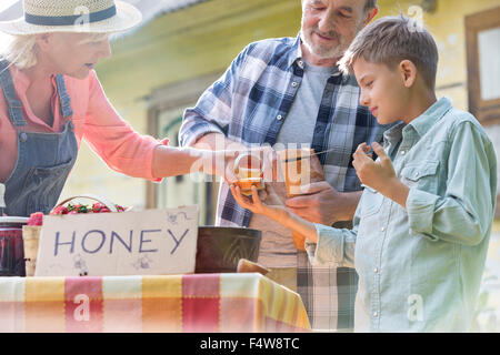 Großeltern und Enkel, Verkostung und Verkauf von Honig an Bauern Marktstand Stockfoto