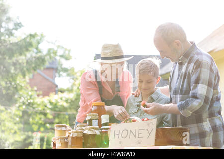 Großeltern und Enkel, Verkauf von Honig an Bauern Marktstand Stockfoto