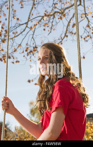 Schweden, Sodermanland, Stigtomta, Teenage Mädchen (14-15) sitzen auf Baum schwingen im Sonnenlicht Stockfoto
