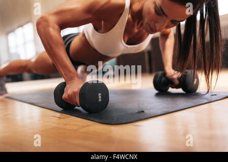 Muskulöse Frau Liegestütze auf Hanteln im Fitnessstudio zu tun. Starke weibliche im Health Club trainieren. Stockfoto