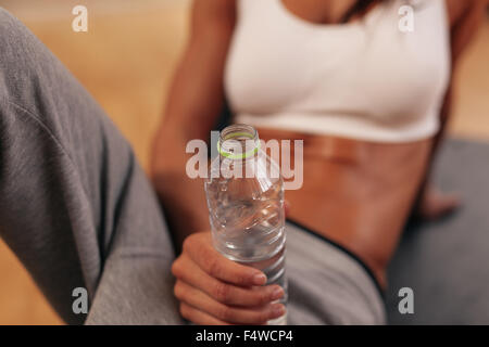 Porträt von Fitness-Frau mit Wasserflasche in Turnhalle hautnah. Flasche Wasser im Mittelpunkt. Stockfoto