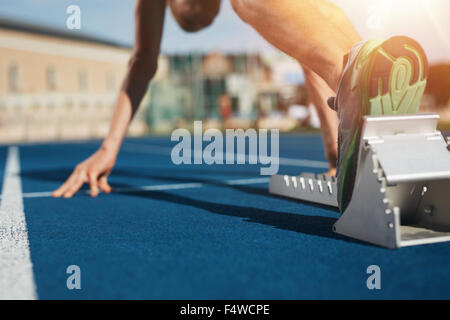 Füße auf Startblock bereit für einen Frühling starten.  Fokus auf Bein eines Athleten kurz vor dem start eines Rennens im Stadion mit Sonne Flare. Stockfoto